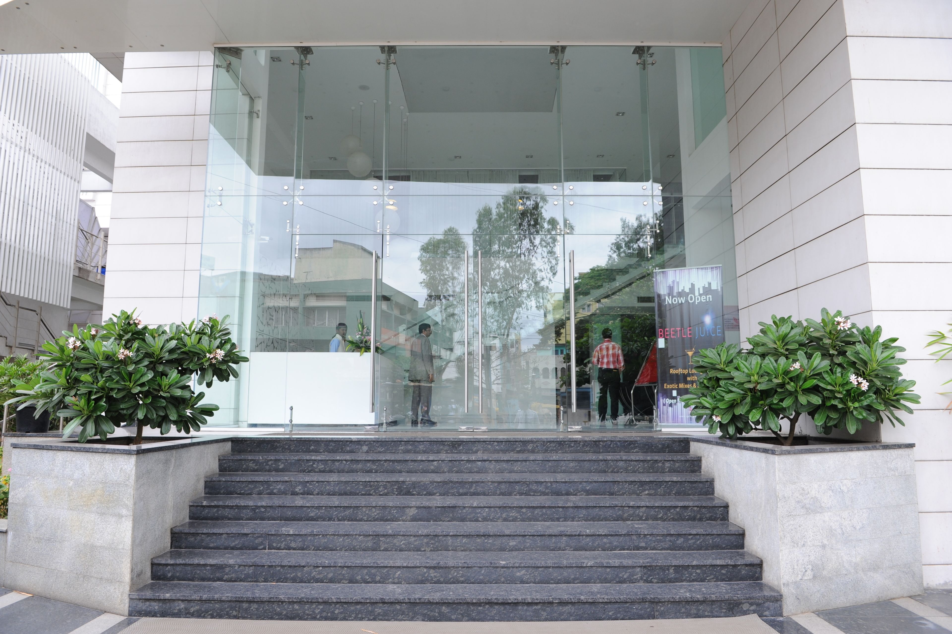 Una entrada moderna de edificio con puertas de vidrio, una escalera y plantas en macetas.