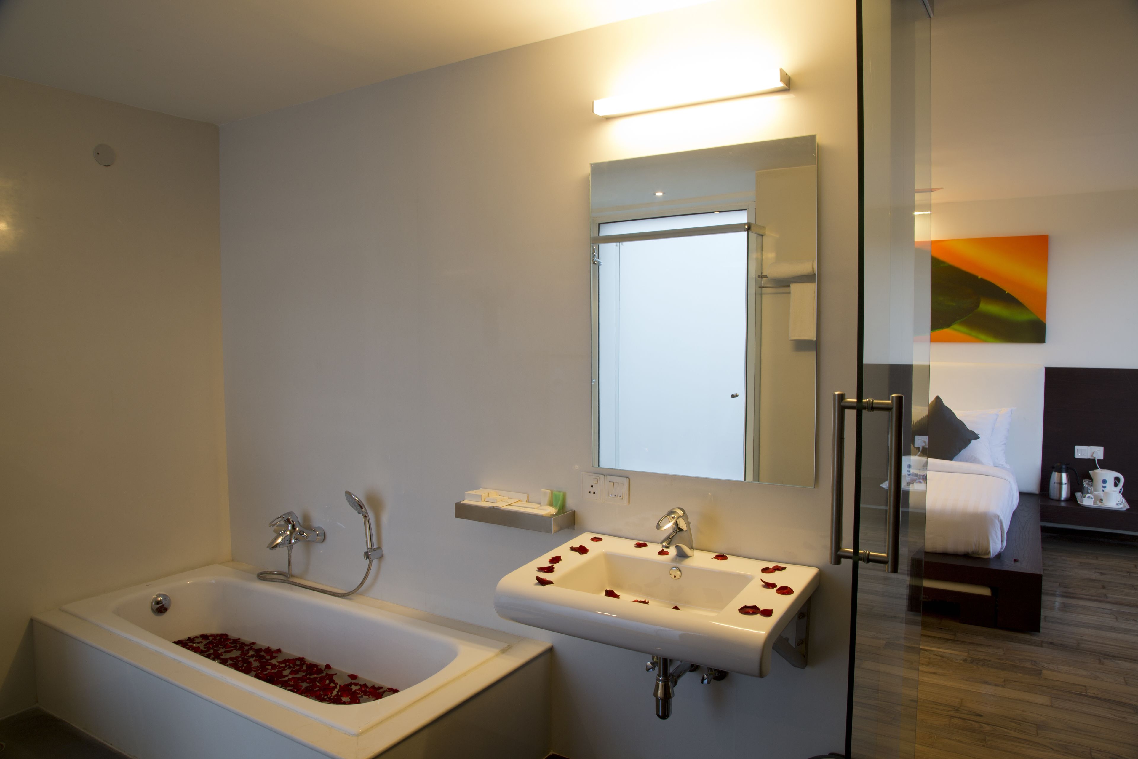 Un baño moderno con una bañera llena de pétalos de rosa, un lavamanos con pétalos de rosa y un espejo sobre el lavamanos.