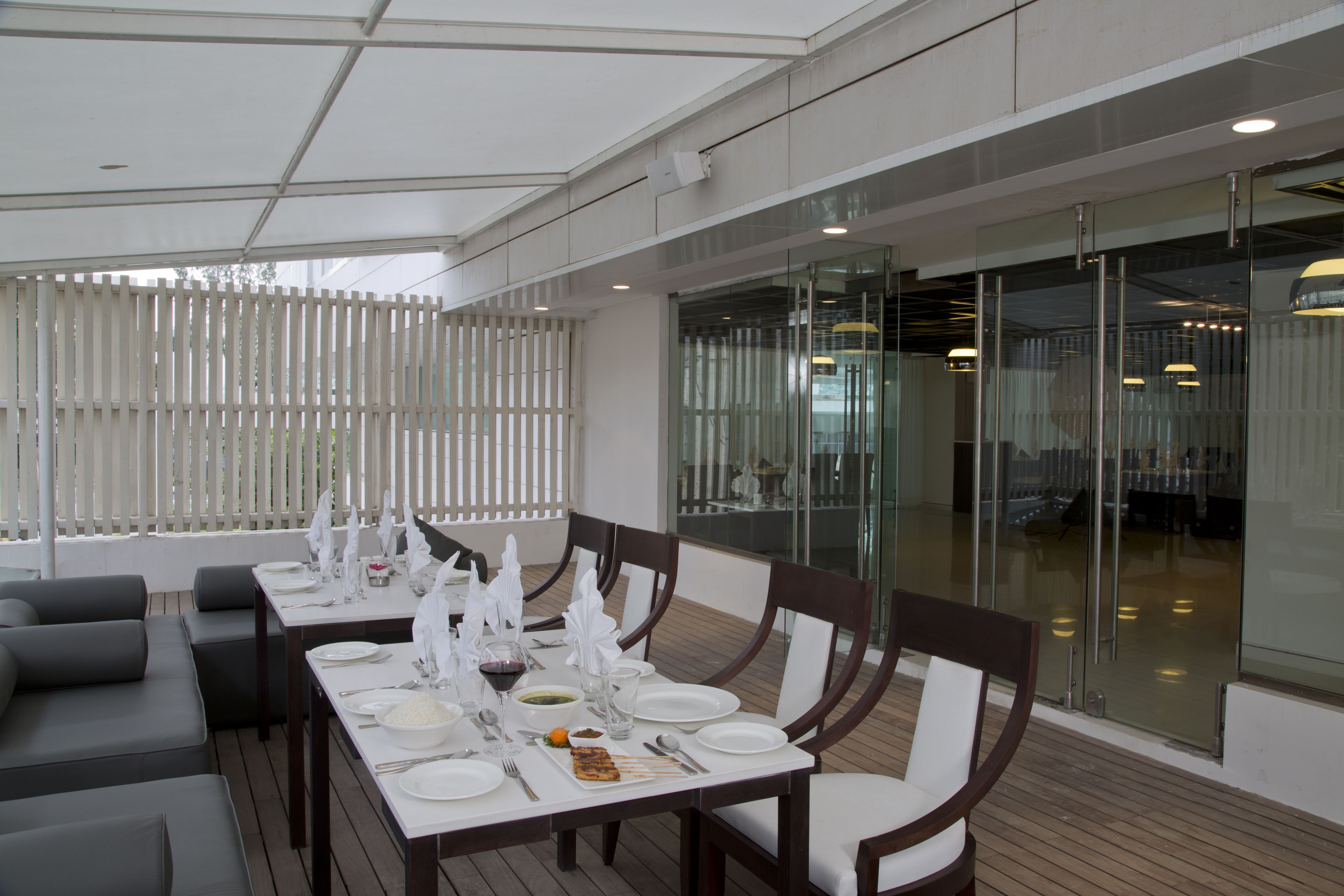 A modern dining area with a long table set for a meal, surrounded by cushioned seating and glass partitions.