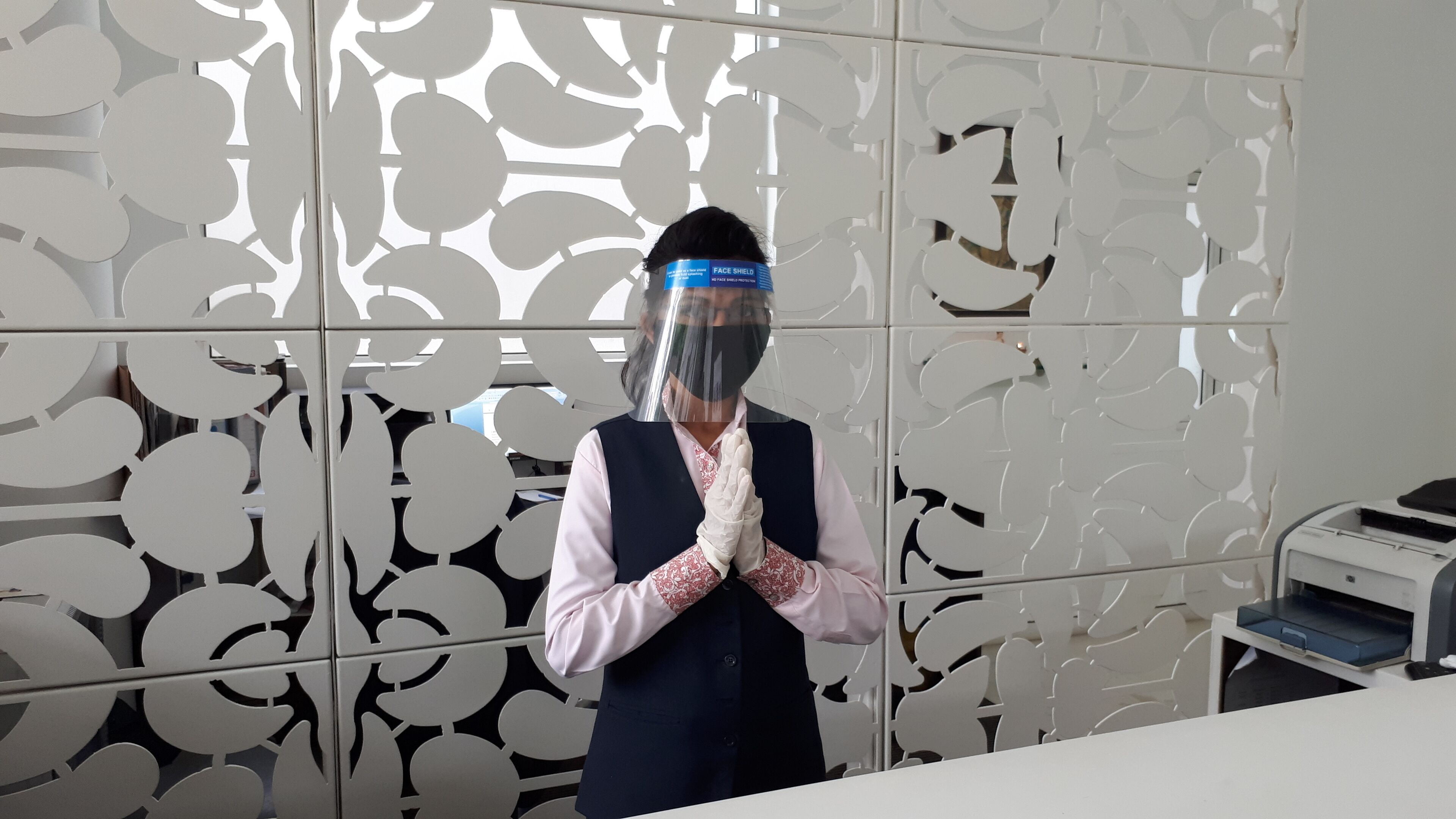 A person in a uniform standing in front of a decorative partition with a pattern of circles and lines.