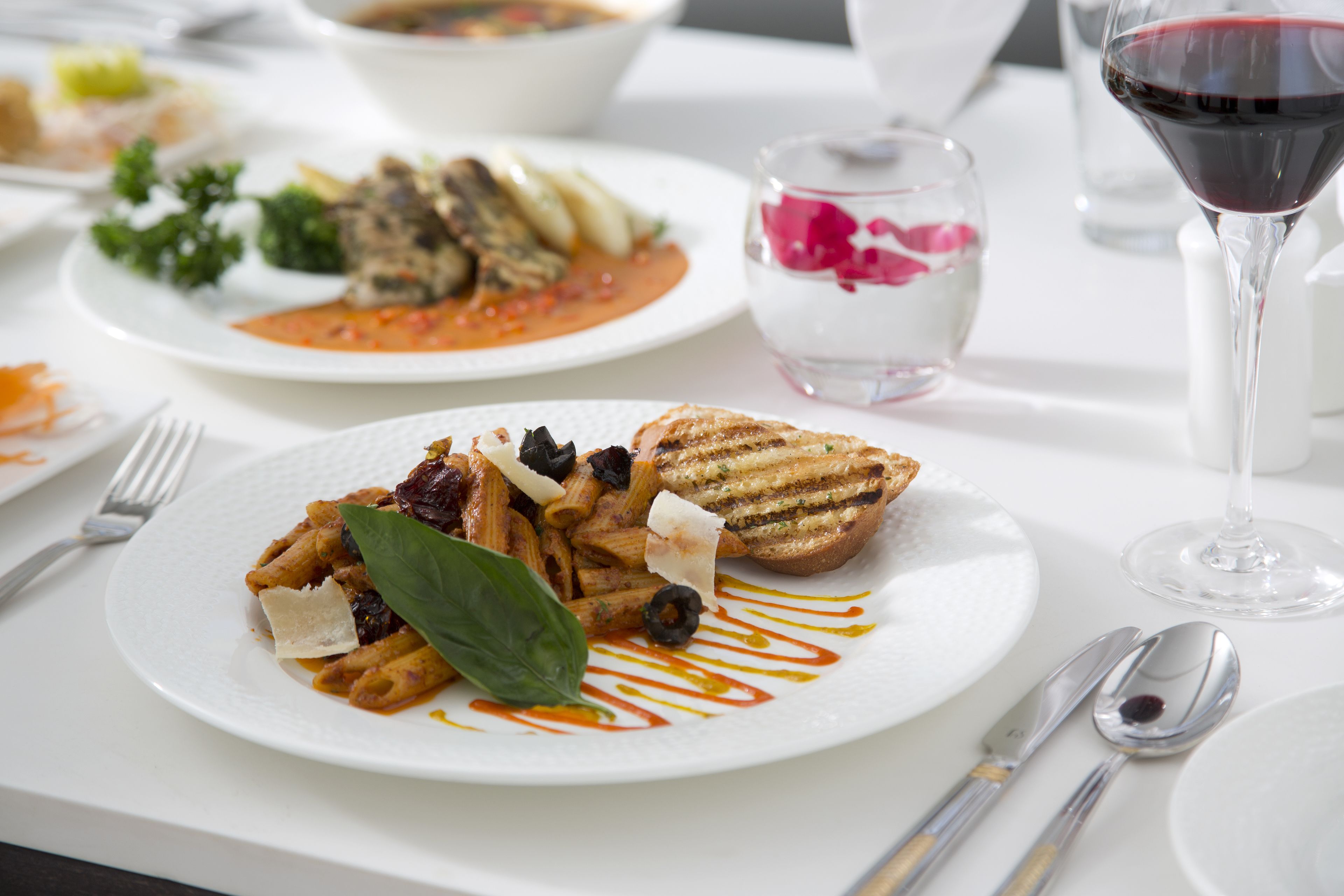 Une table à manger avec des assiettes de pâtes, un verre de vin rouge et des couverts.