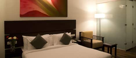 A hotel room with a large bed, a nightstand with a vase of flowers, a chair, a desk, and a wardrobe.