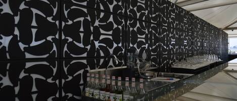Un espace bar avec un mur aux motifs géométriques modernes en noir et blanc, un comptoir en verre et diverses bouteilles et verres.