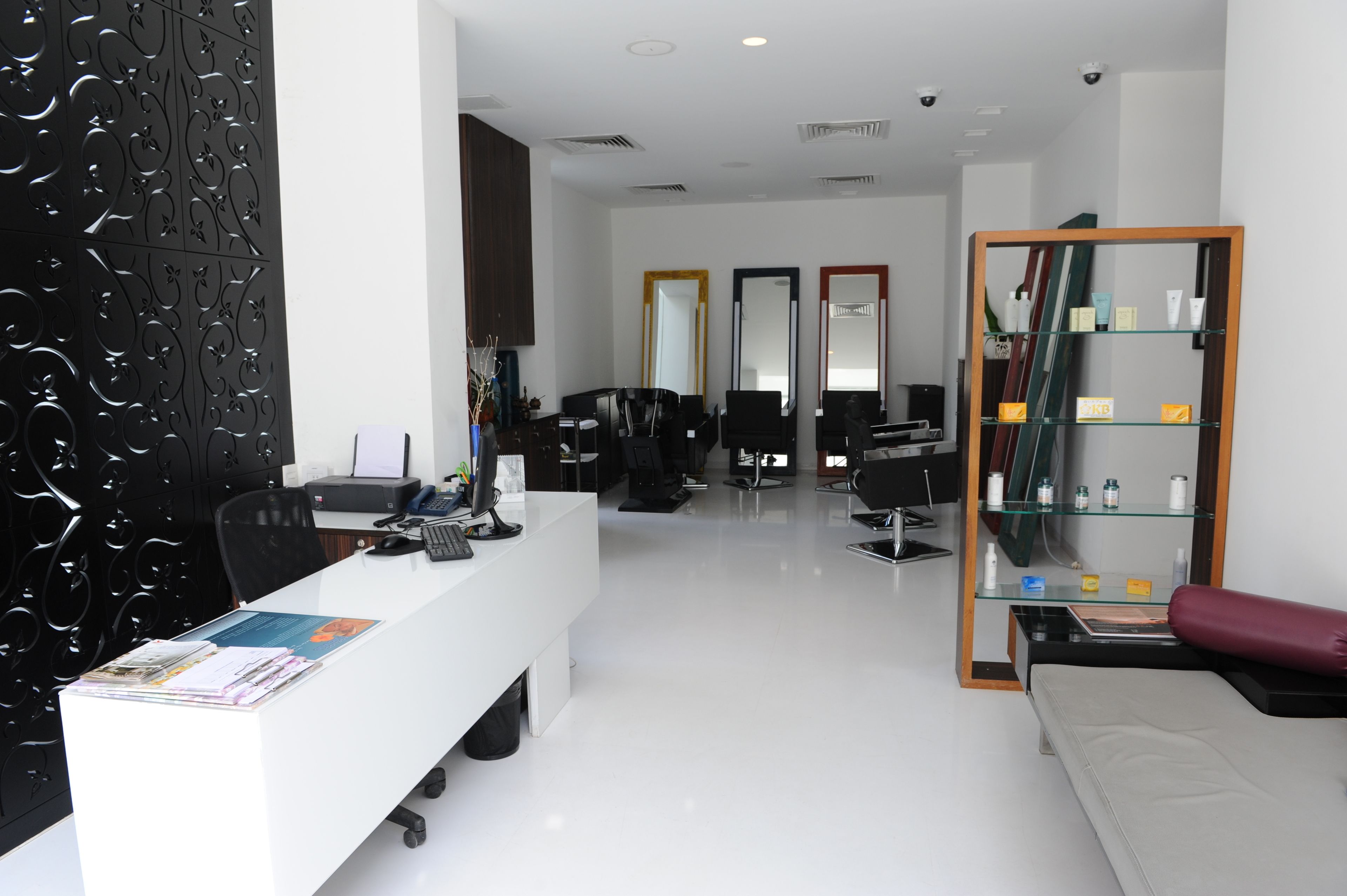 Un salón moderno con un mostrador de recepción blanco, sillas negras y una vitrina de vidrio con productos.