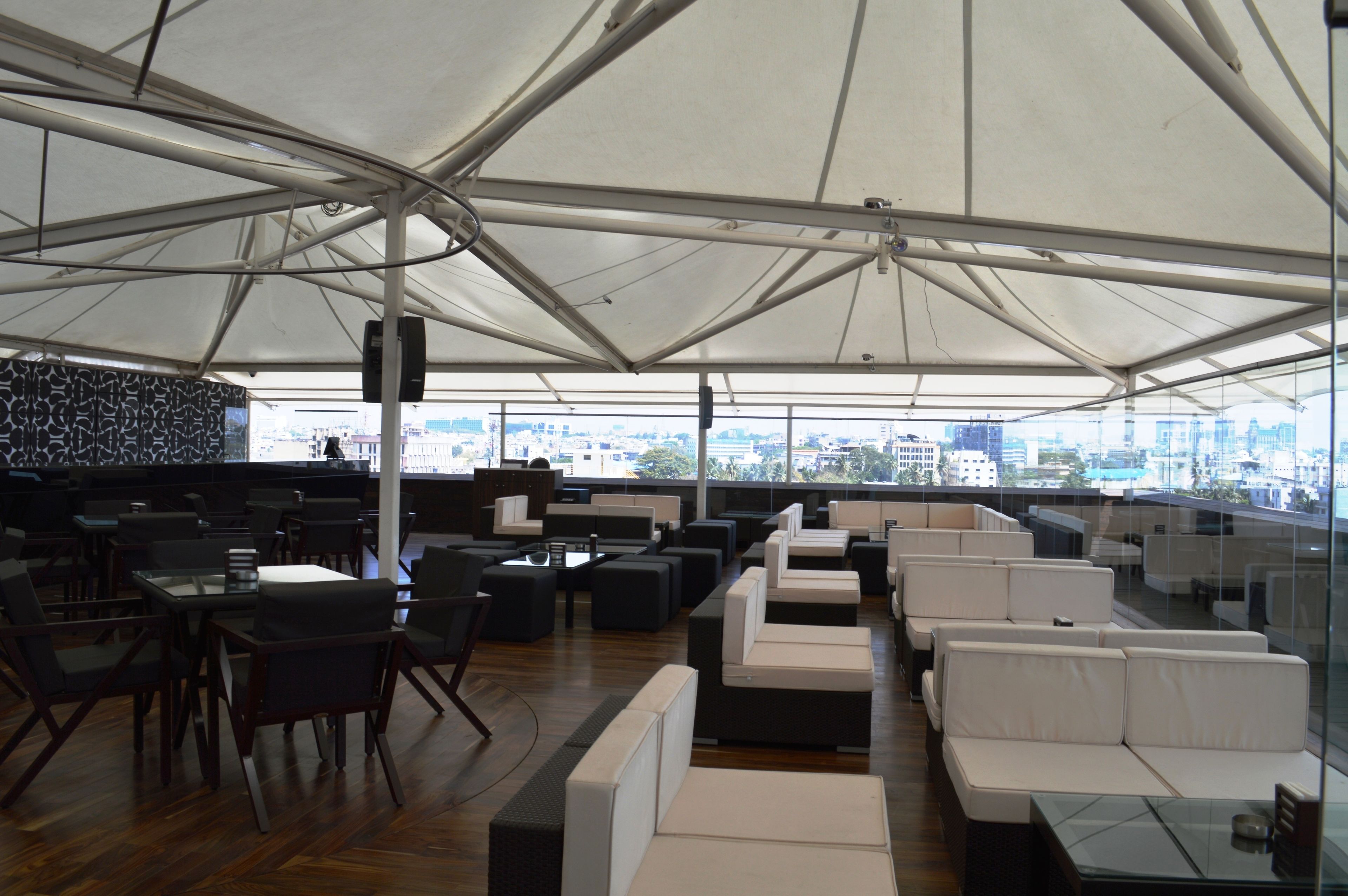 A rooftop bar with a view of the city skyline, featuring modern seating and a large tent structure.