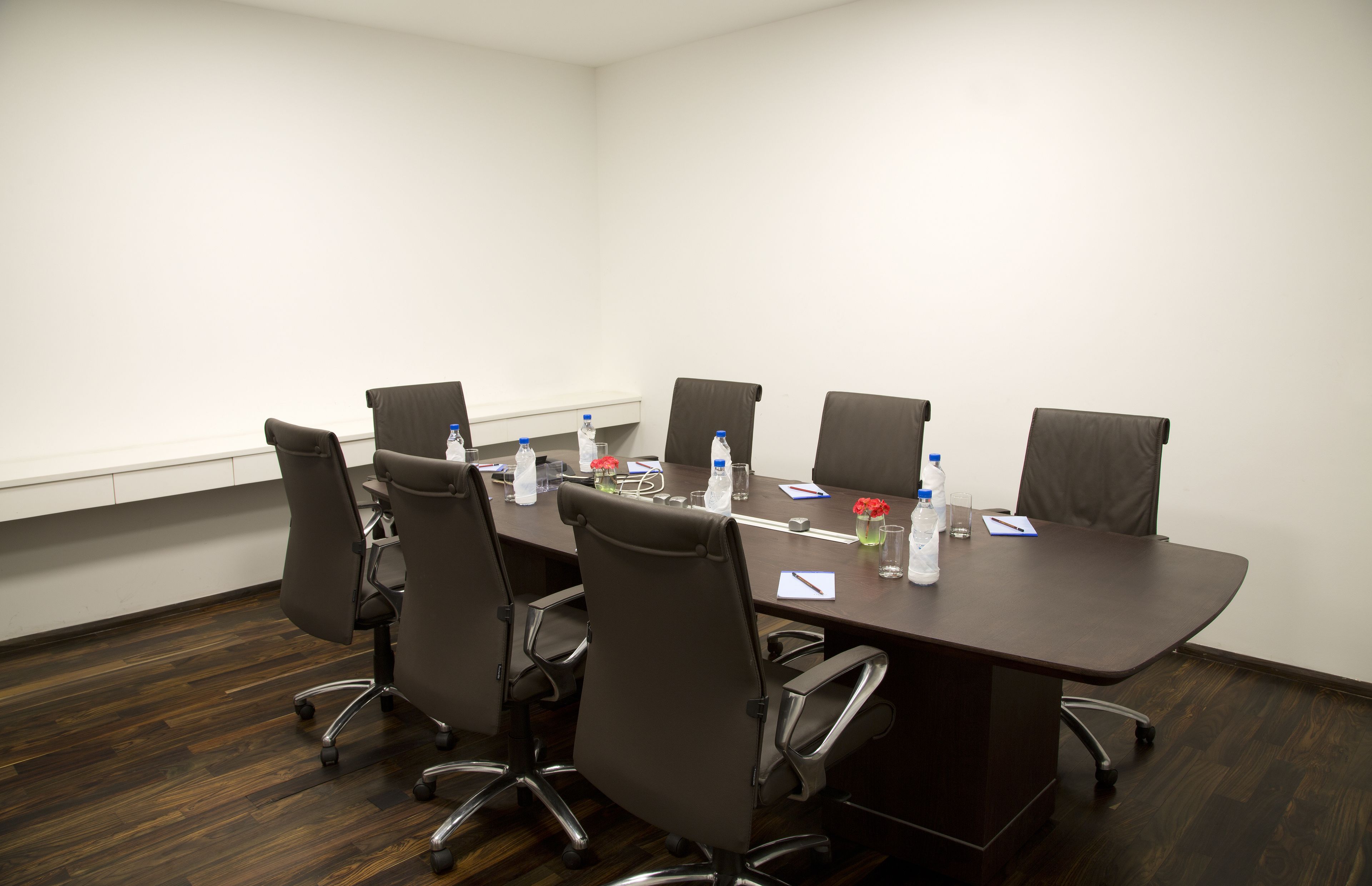 Sala de conferência com uma mesa comprida, seis cadeiras e diversos itens como garrafas de água e documentos.