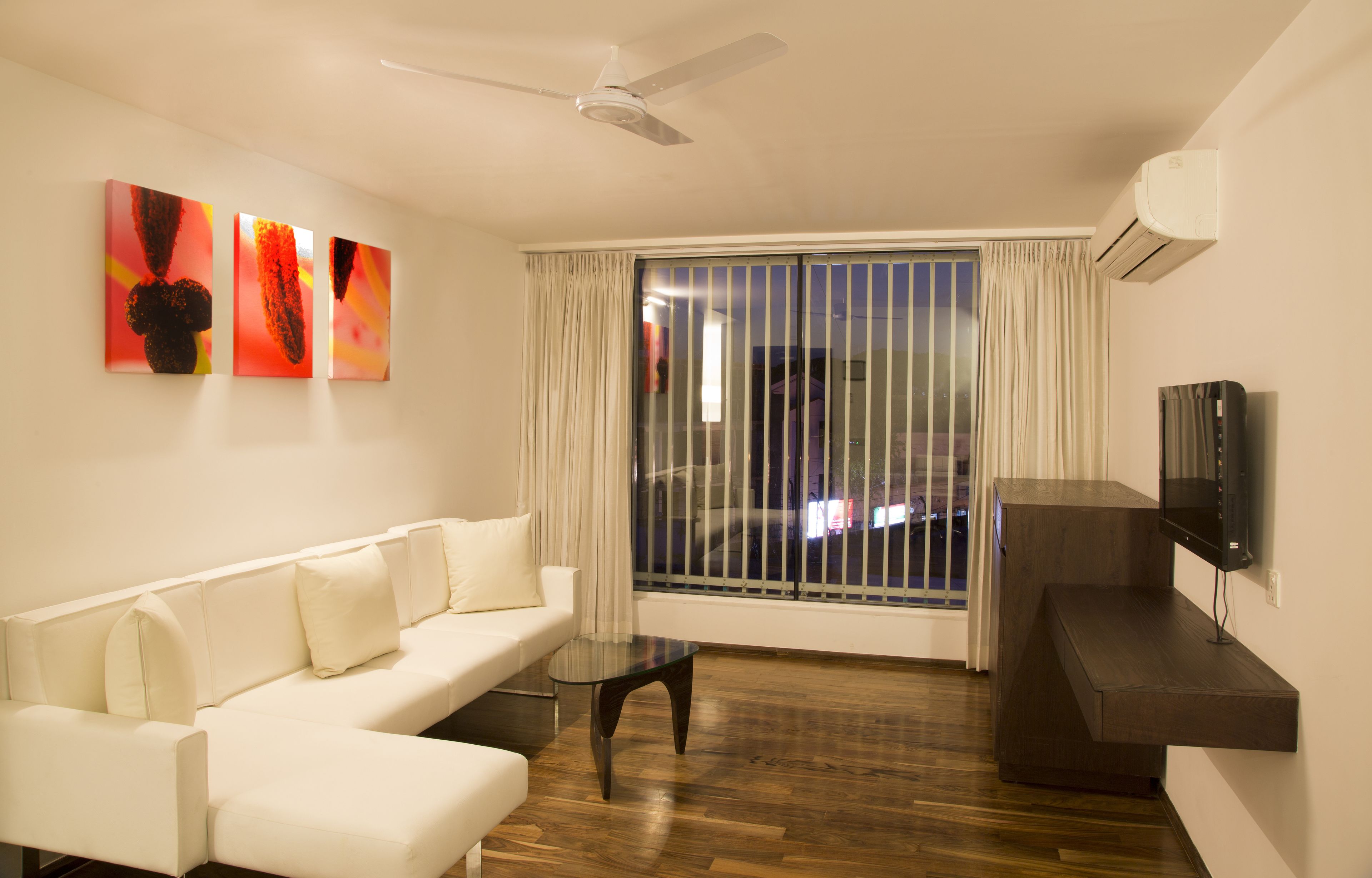 A modern living room with a white sofa, a glass coffee table, and a flat-screen TV mounted on the wall.