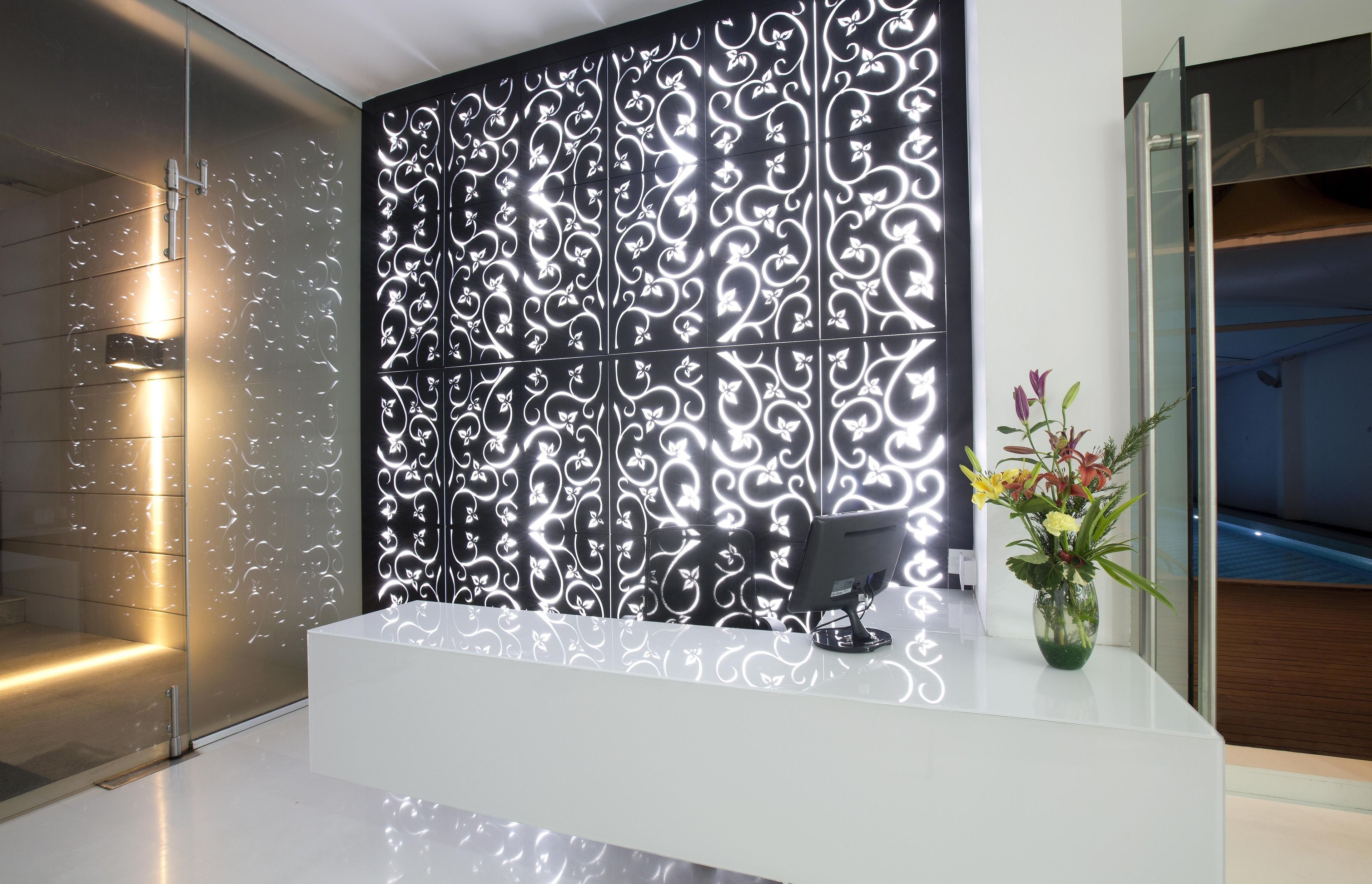 A modern reception area with a white reception desk, a decorative black panel with white patterns, and a vase with flowers.