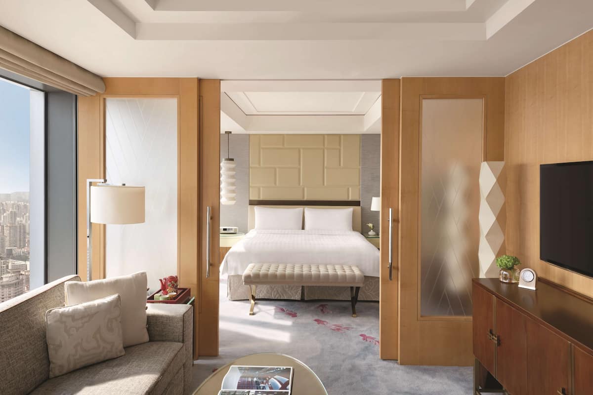 Una habitación de hotel moderna con una cama grande, un sofá, un televisor y vistas a la ciudad.