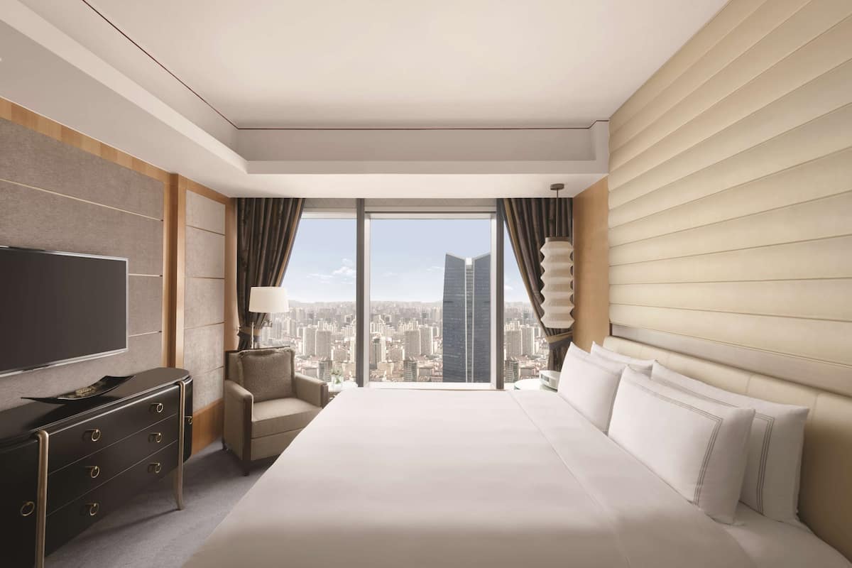Una habitación de hotel moderna con una cama grande, un televisor de pantalla plana, un aparador y vistas a la ciudad.