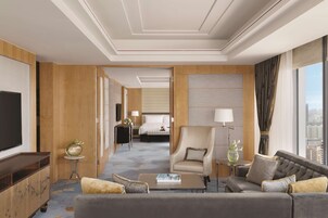 A hotel room with a large flat-screen TV, a sofa, a coffee table, a chair, a bed, and a view of the city.