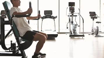 Une personne utilise un appareil de musculation pour les jambes dans une salle de sport, avec divers autres équipements d'exercice en arrière-plan.