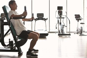 A person using a leg press machine in a gym with various exercise equipment in the background.