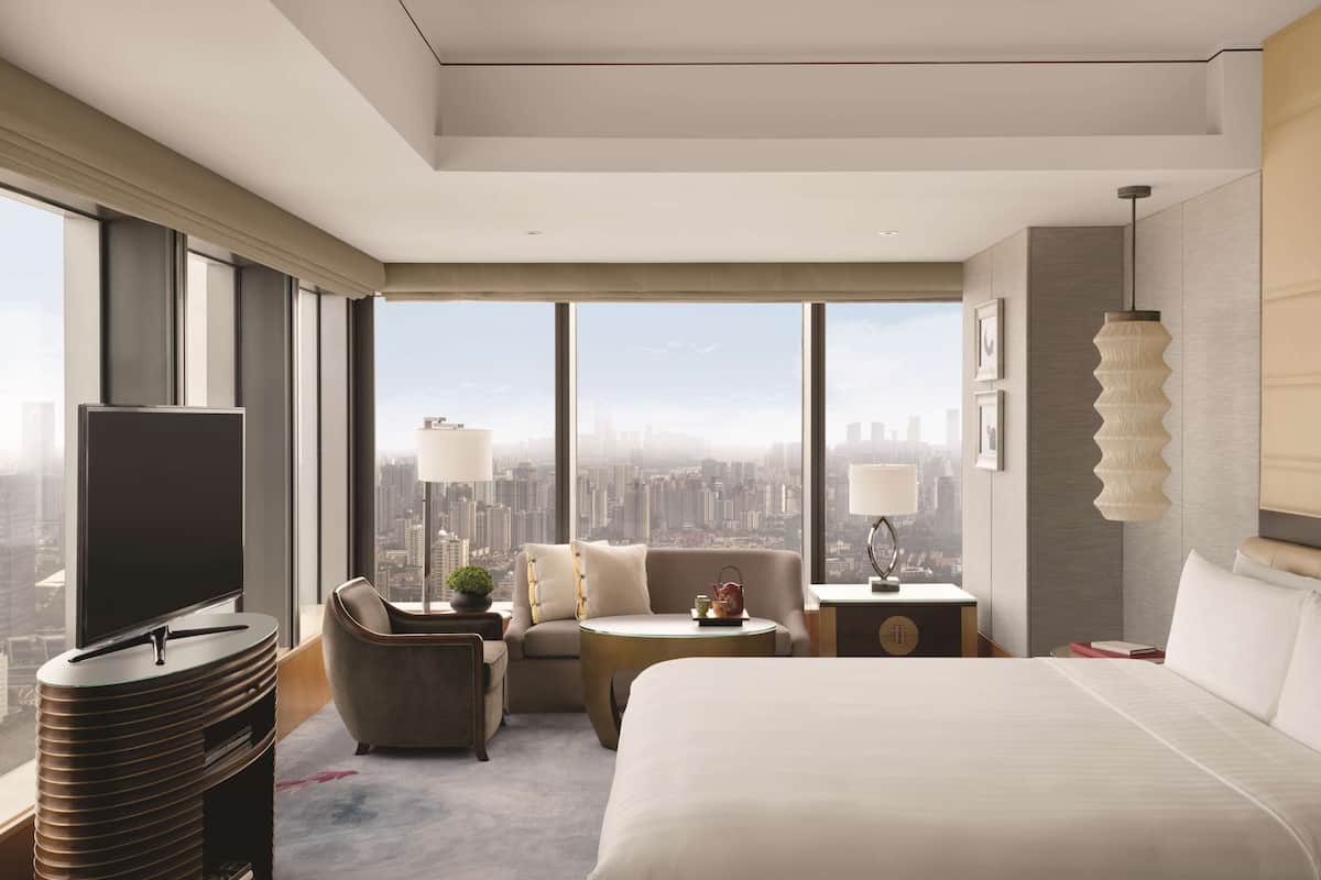 Una habitación de hotel moderna con una cama grande, un sofá, una mesita, un televisor y vistas a la ciudad.