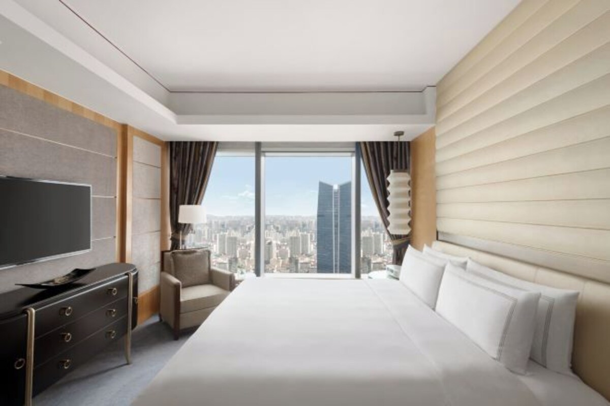 Una habitación de hotel moderna con una cama grande, un televisor de pantalla plana, un aparador y vistas a la ciudad.