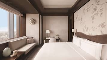 A modern hotel room with a large bed, a seating area, a desk, and a view of the city.