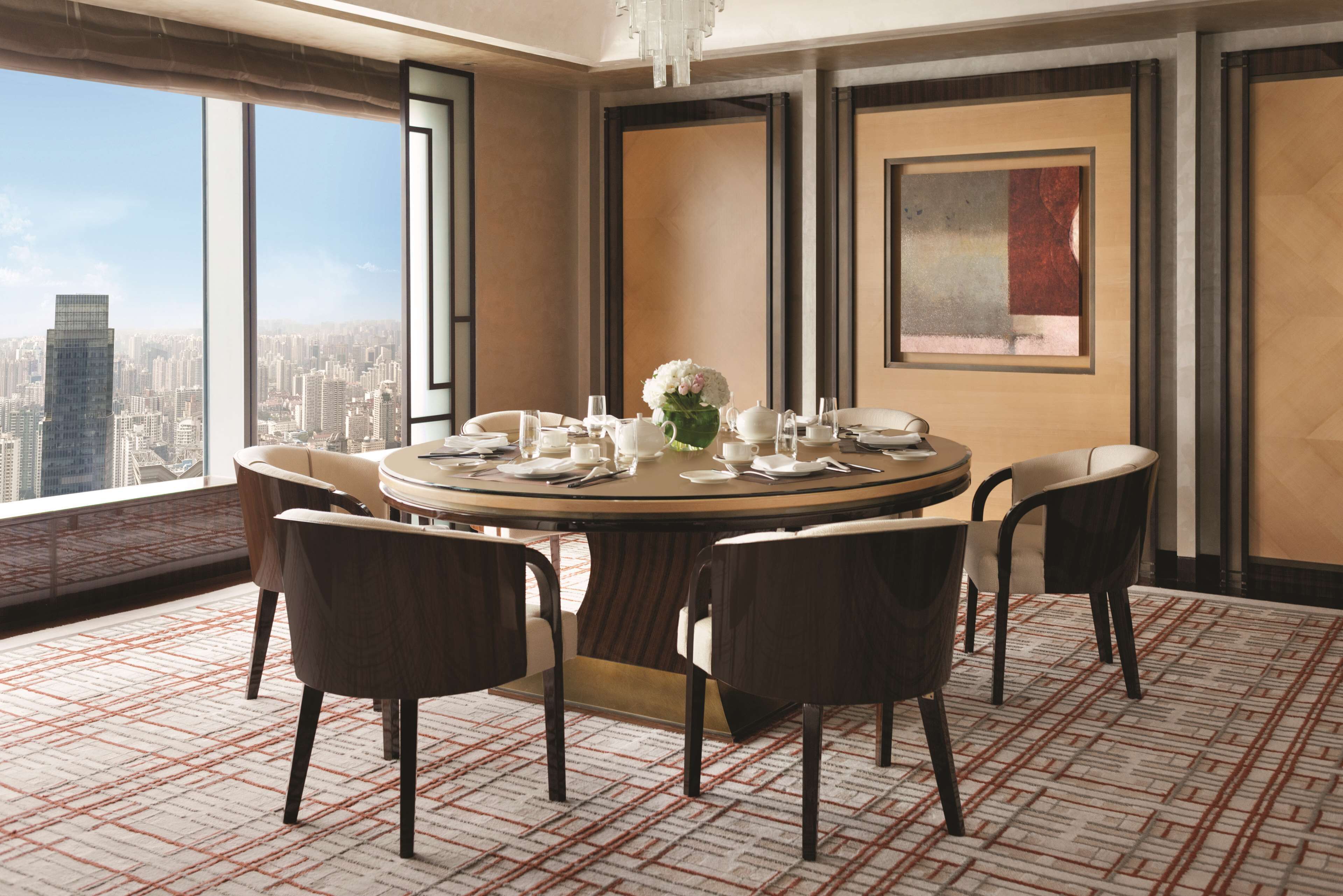 A dining room with a round table, six chairs, and a city view through large windows.
