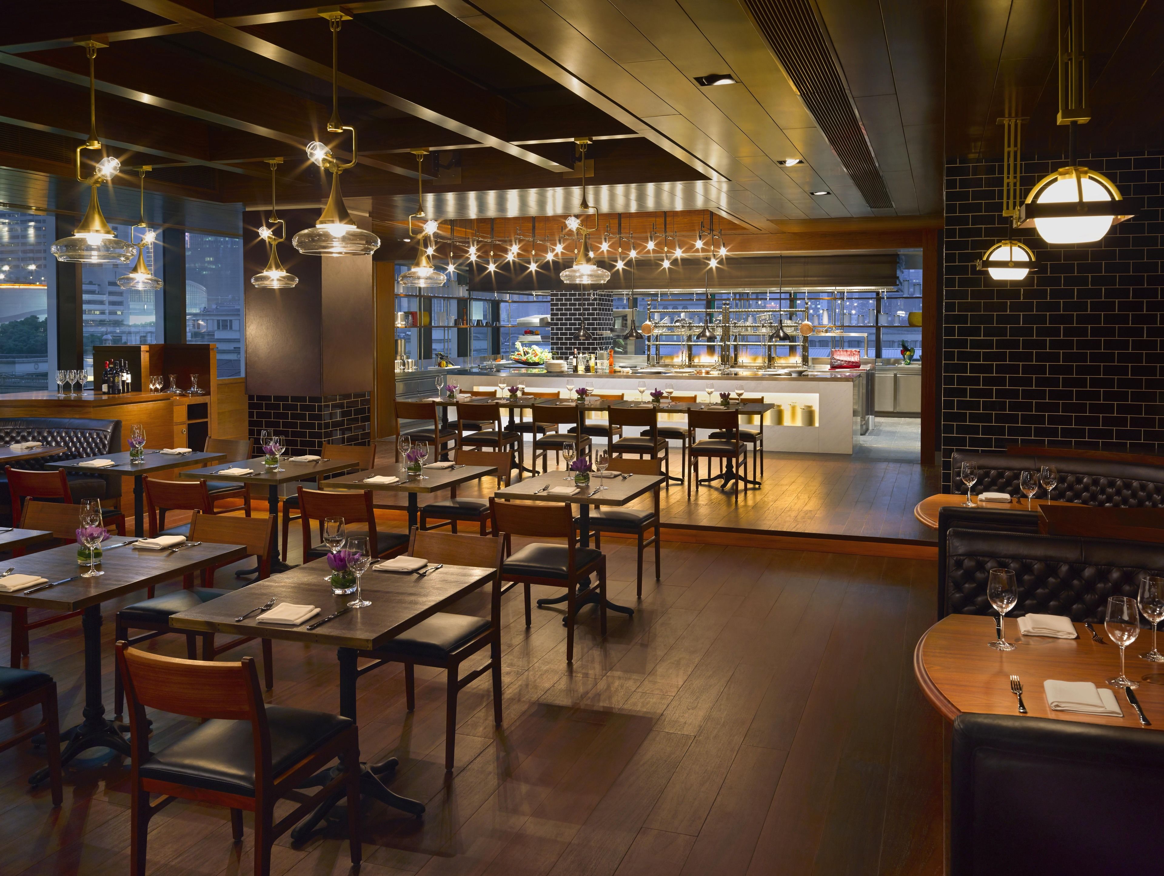 Ein Restaurant mit mehreren Tischen, Sitzecken und einer Bar, mit Blick auf die Stadt durch große Fenster.