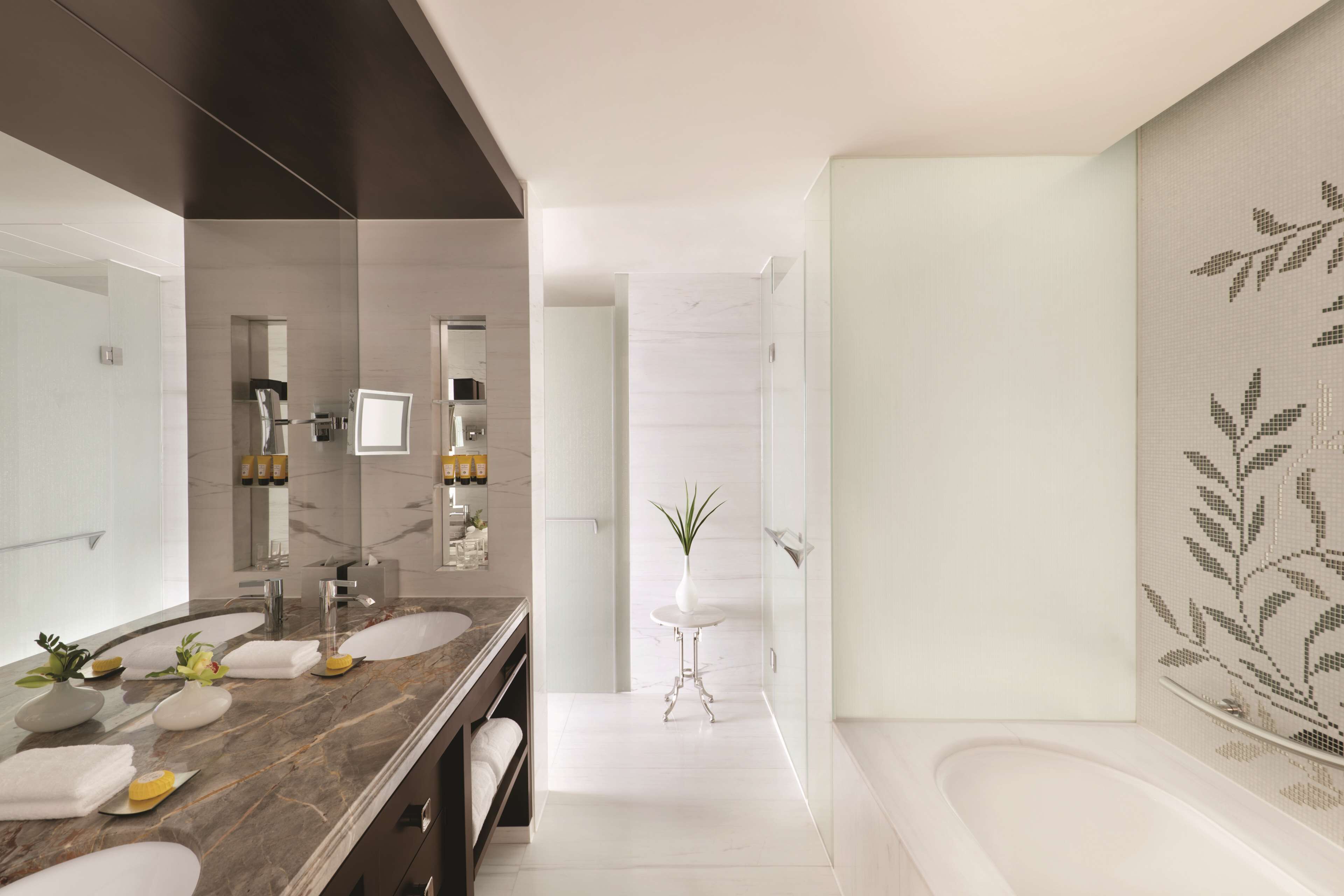 Un baño moderno con tocador de mármol, un espejo grande, cabina de ducha de vidrio y una planta decorativa.