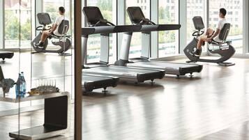 A gym with treadmills and elliptical machines, large windows, and a wooden floor.