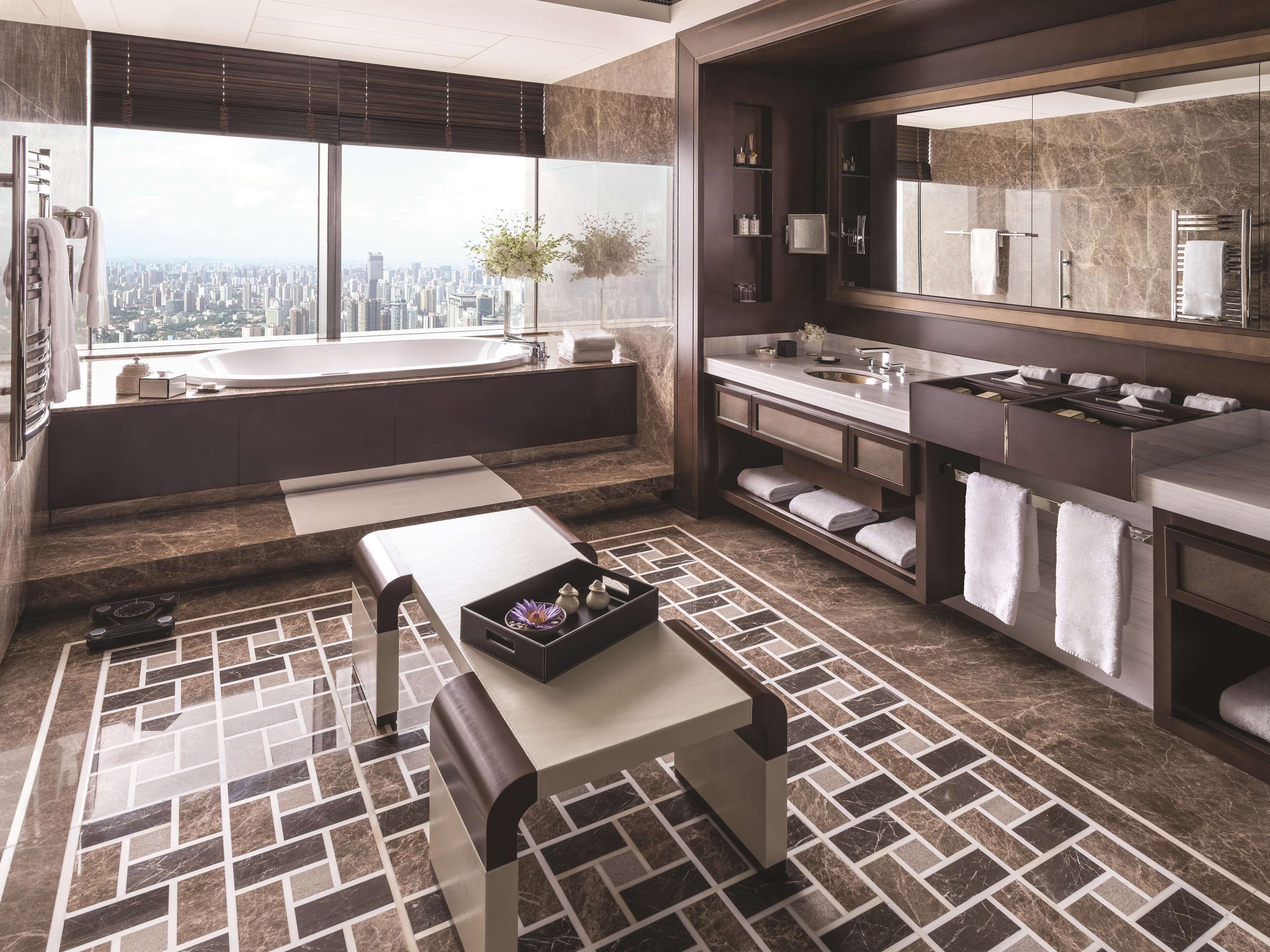A modern bathroom with a large bathtub, a vanity with a mirror, and a view of the city.
