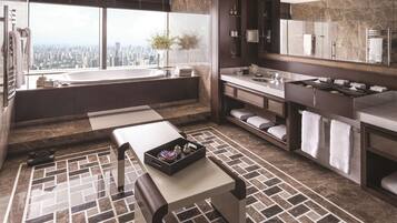 A modern bathroom with a large bathtub, a vanity with a mirror, and a view of the city.