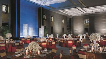 A banquet hall with round tables, red and gold chairs, and white floral centerpieces.