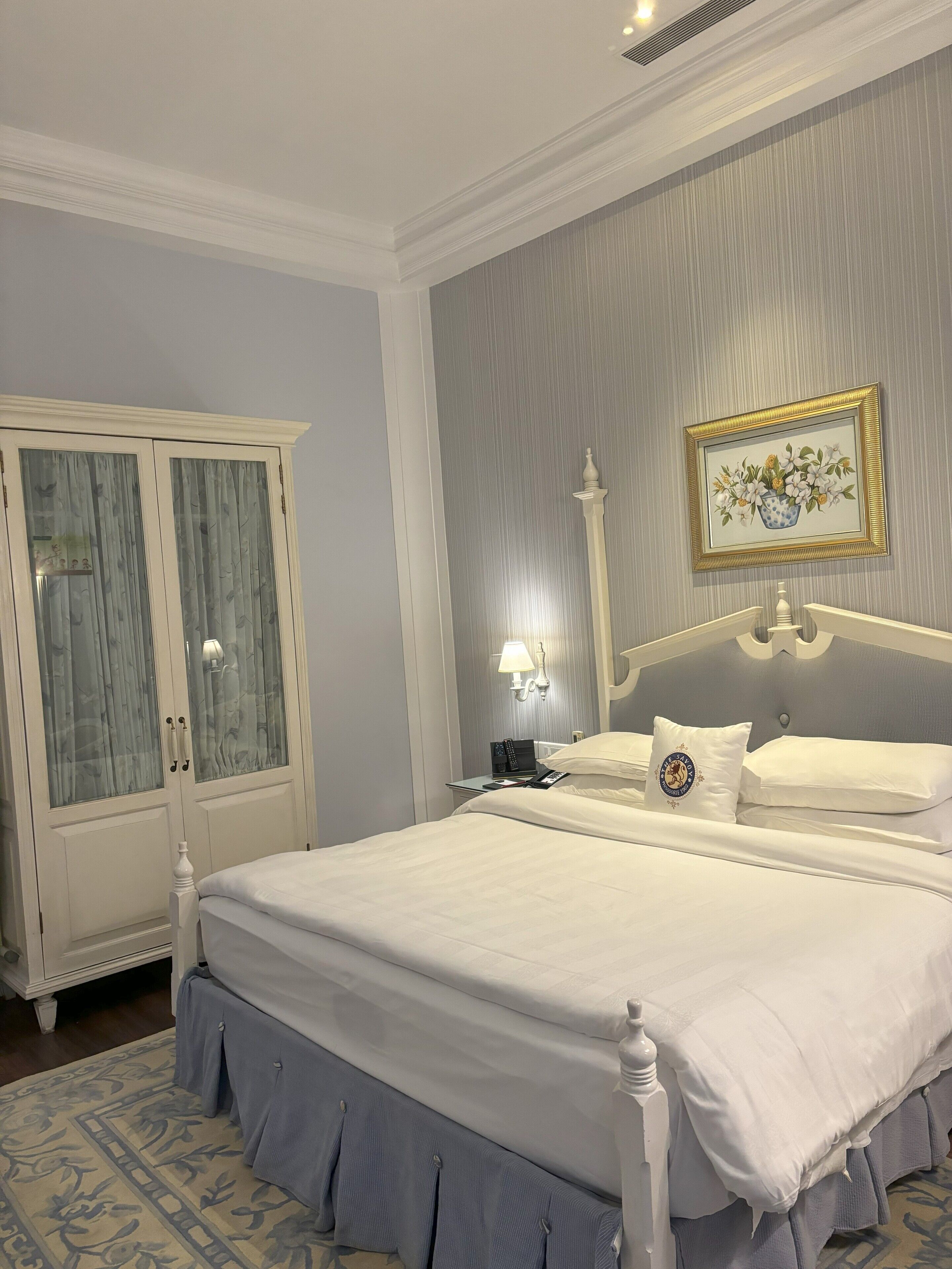 A neatly made bed with white linens, a bedside table with a lamp, and a framed picture on the wall.