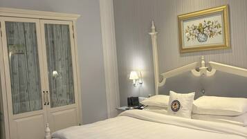 A neatly made bed with white linens, a bedside table with a lamp, and a framed picture on the wall.