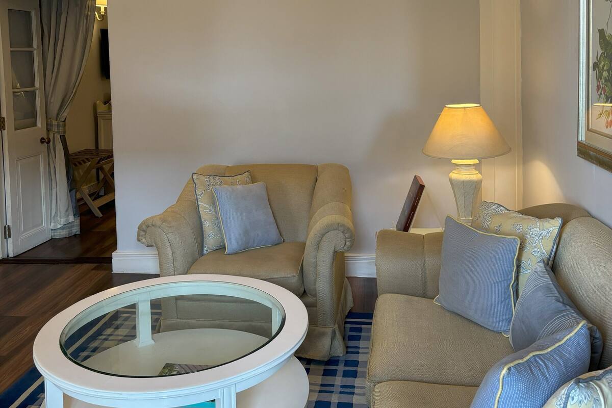 A living room with a beige sofa set, a round coffee table, a floor lamp, and a framed picture on the wall.