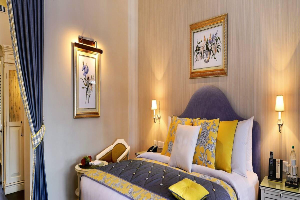 A hotel room with a bed, bedside tables, a nightstand, a lamp, a framed picture on the wall, and a curtain.