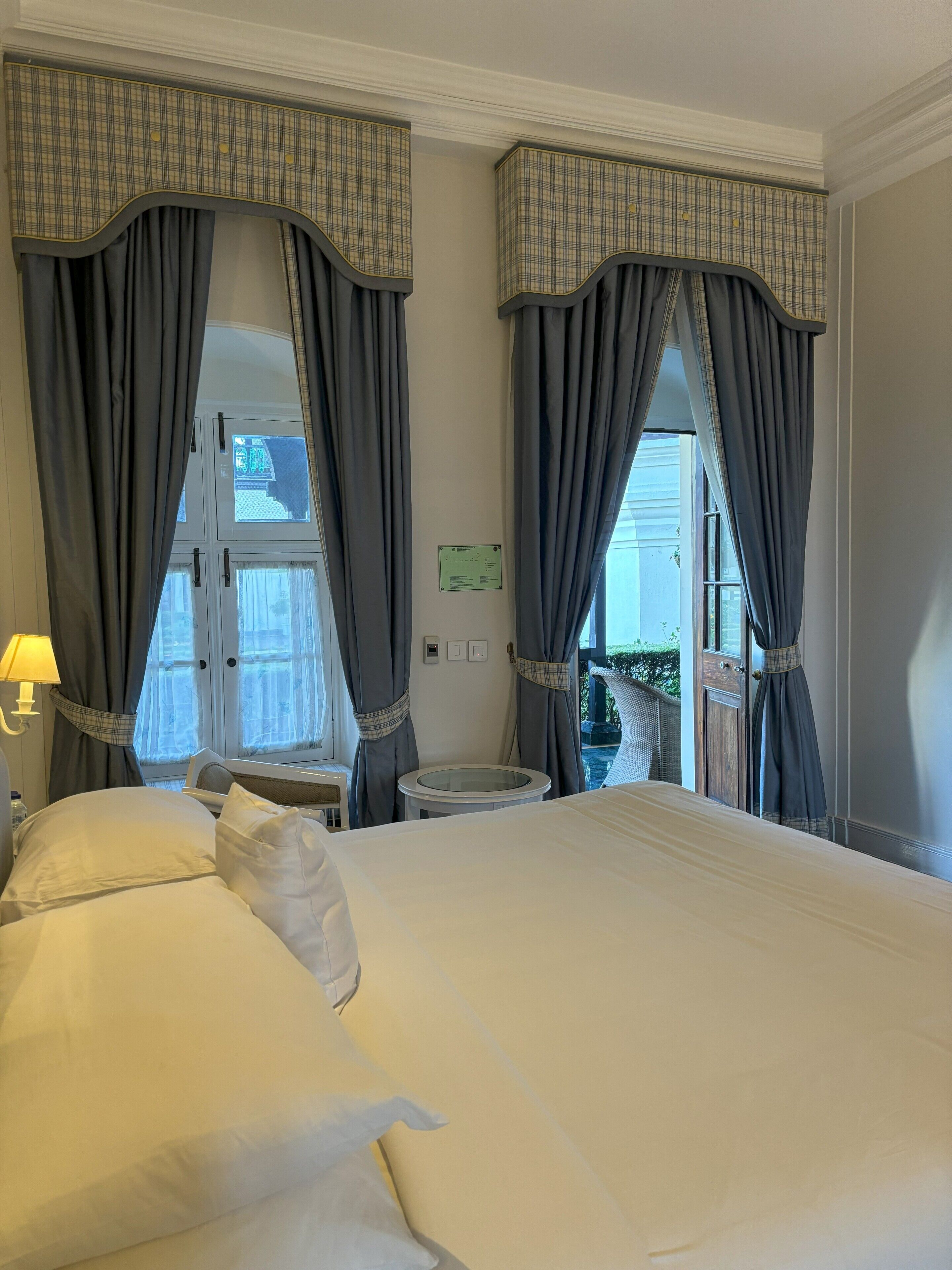A hotel room with a large bed, grey curtains, a small round table, and a window with a view.