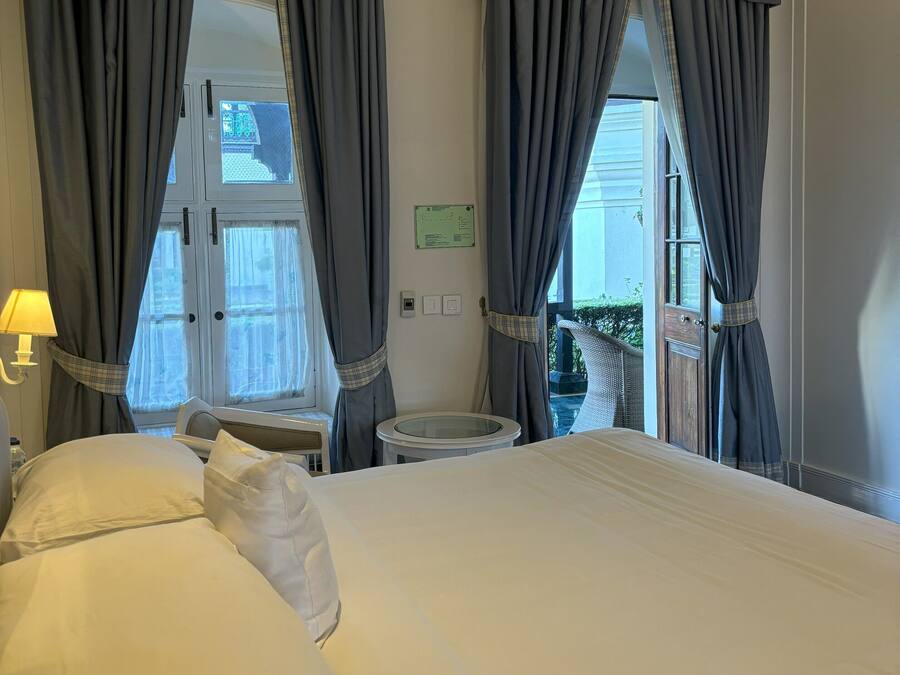 A hotel room with a large bed, grey curtains, a small round table, and a window with a view.
