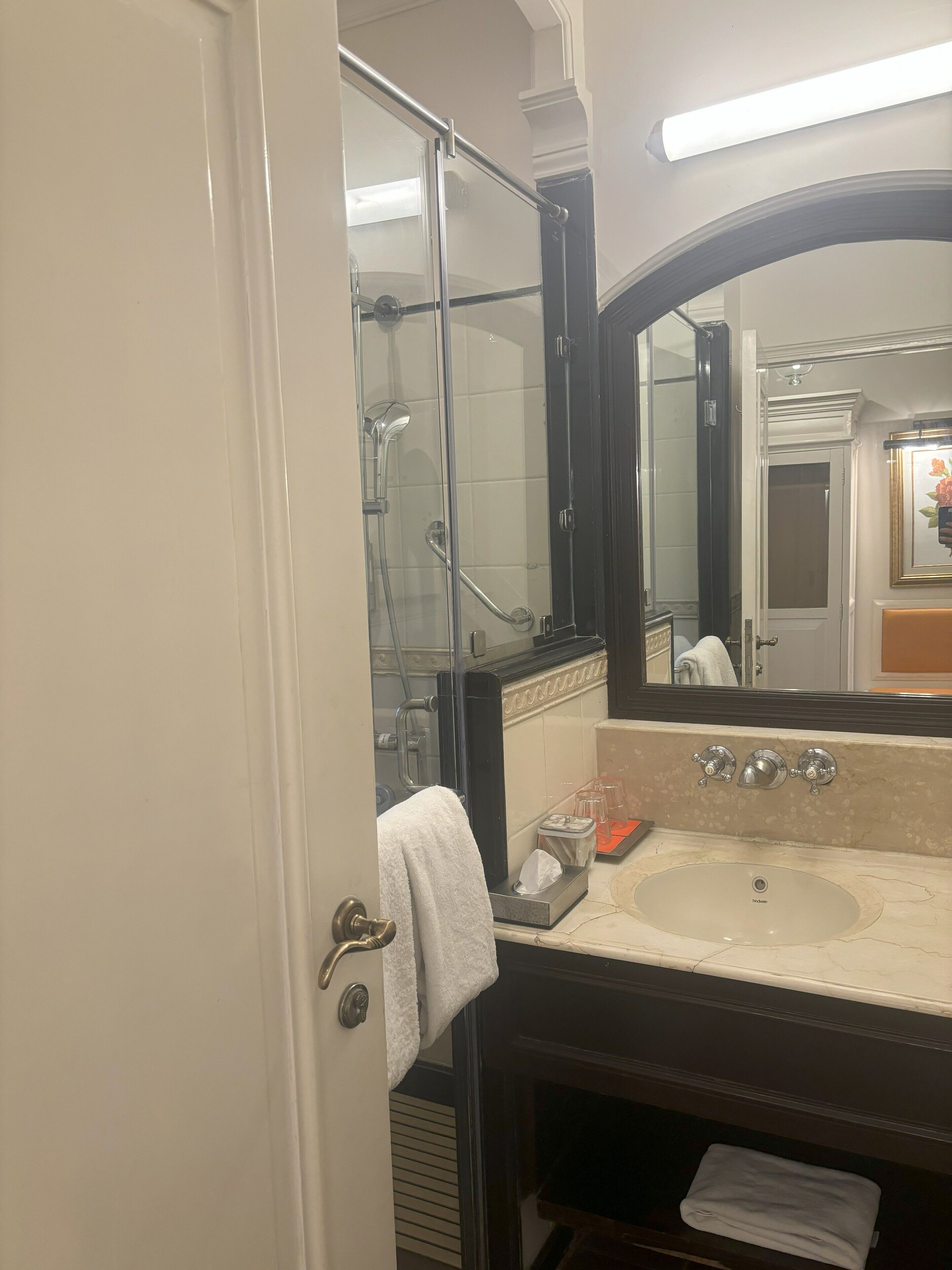 A bathroom with a glass shower enclosure, a sink with a marble countertop, and a large mirror above the sink.