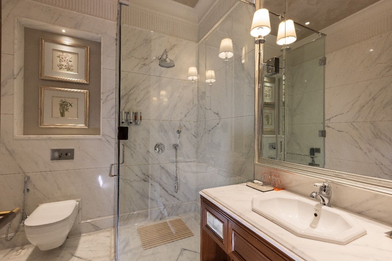 A modern bathroom with a glass-enclosed shower, a large mirror, and a marble-tiled wall.