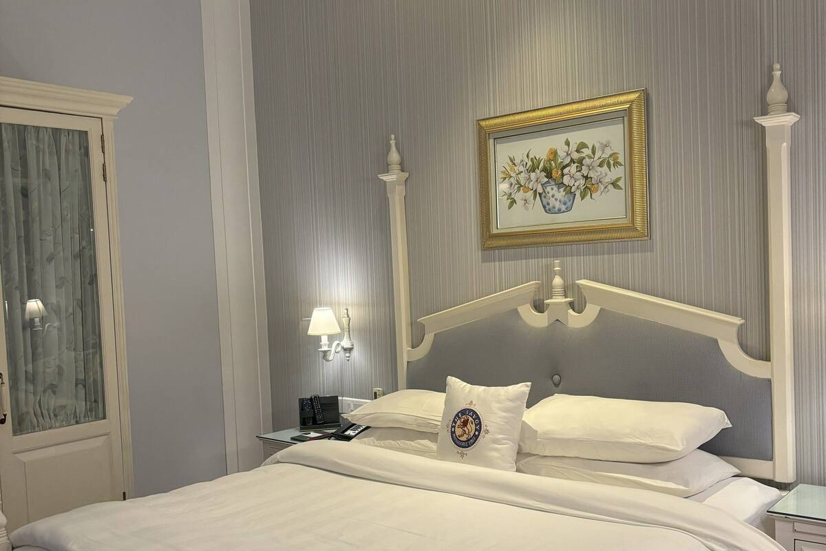 A neatly made bed with a white headboard, a bedside table with a lamp, and a framed picture on the wall.