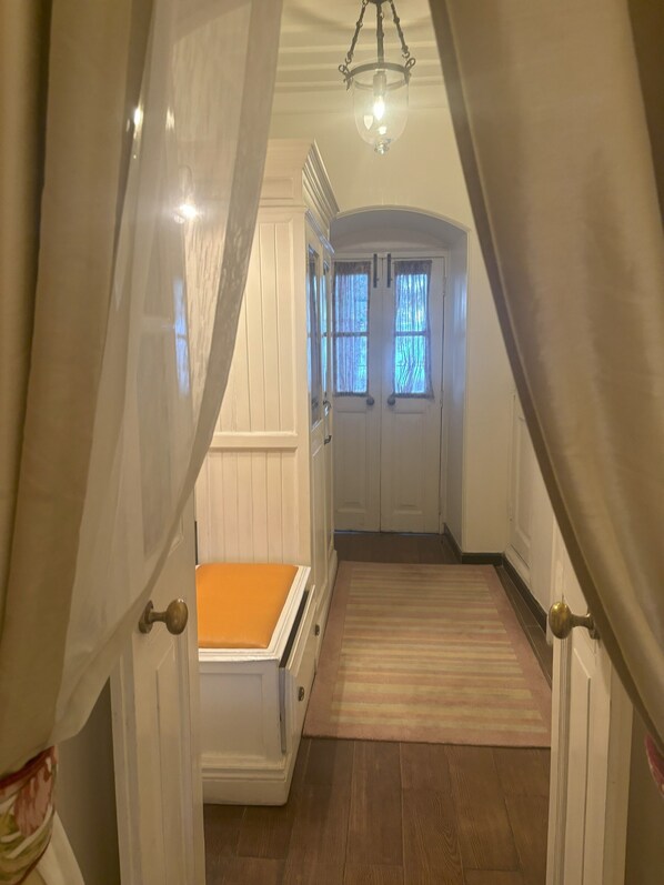 A narrow hallway with a wooden floor, white walls, and a door at the end.