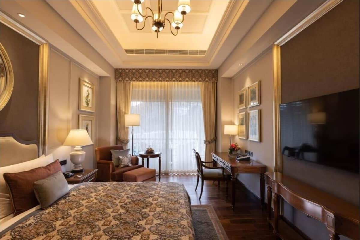 A hotel room with a large bed, a desk, a chair, a television, and a window with curtains.
