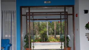 A hotel entrance with an exit sign, a blue chair, and potted plants. - Maistros Hotel Apartments (Protaras)