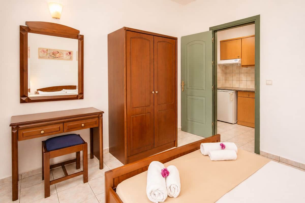 A hotel room with a bed, a desk, a wardrobe, and a green door leading to a kitchen.