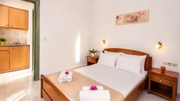 Una habitación de hotel con cama, mesitas de noche, una lámpara de pared, una pequeña planta en maceta y un cuadro.