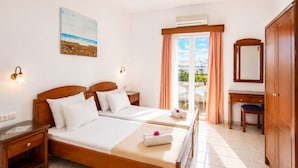 A hotel room with two beds, a desk, a chair, a wardrobe, a window with curtains, an air conditioning unit, and a painting on the wall. - Astir Studios (Hersonissos)