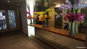 A reception area with a wooden reception desk, glass vases with flowers, and a mirror reflecting the space. - Ace Hotel & Suites (Pasig)