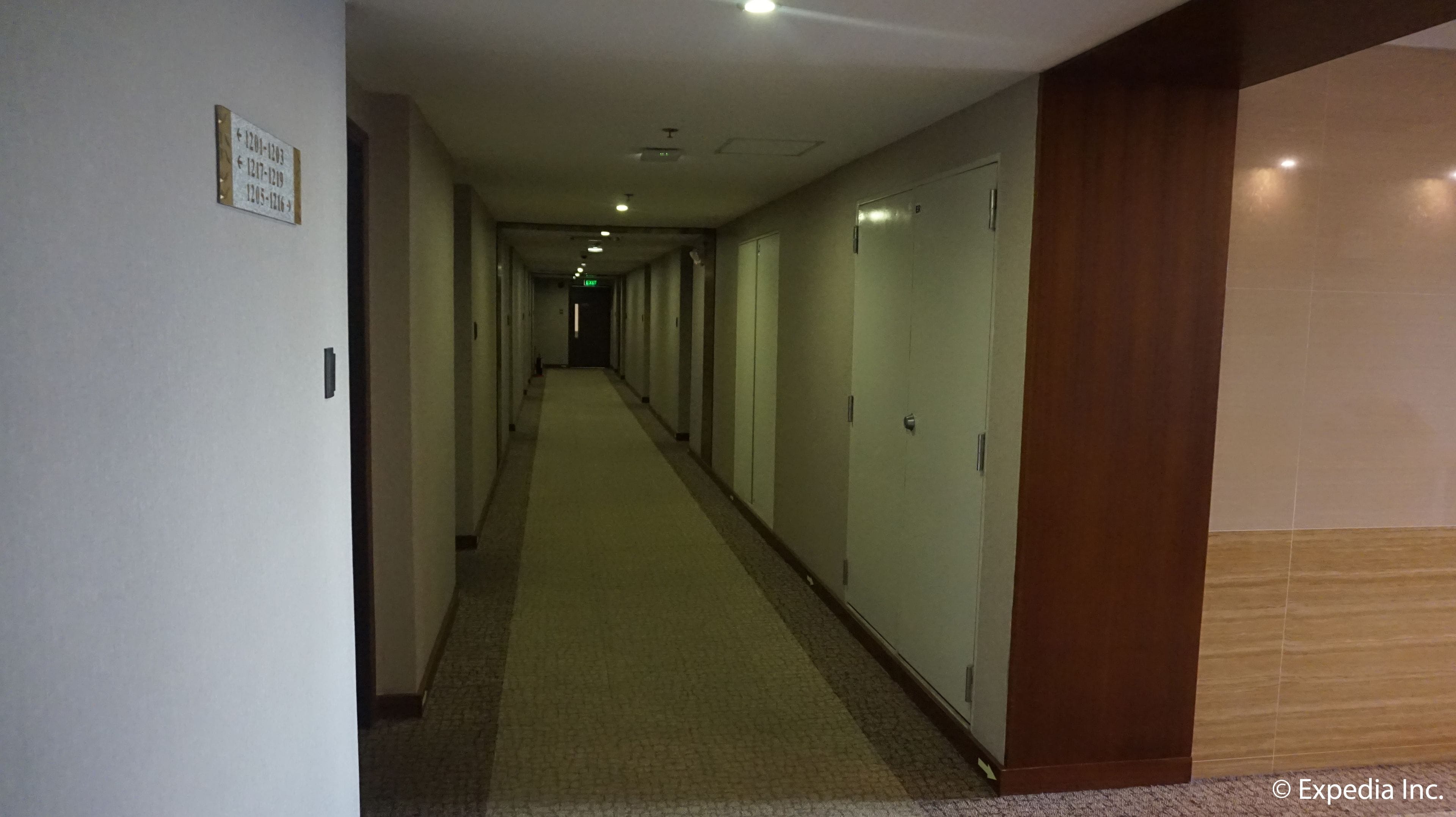 A long, narrow hotel corridor with doors on one side and a carpeted floor.