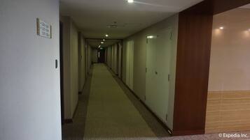 A long, narrow hotel corridor with doors on one side and a carpeted floor.