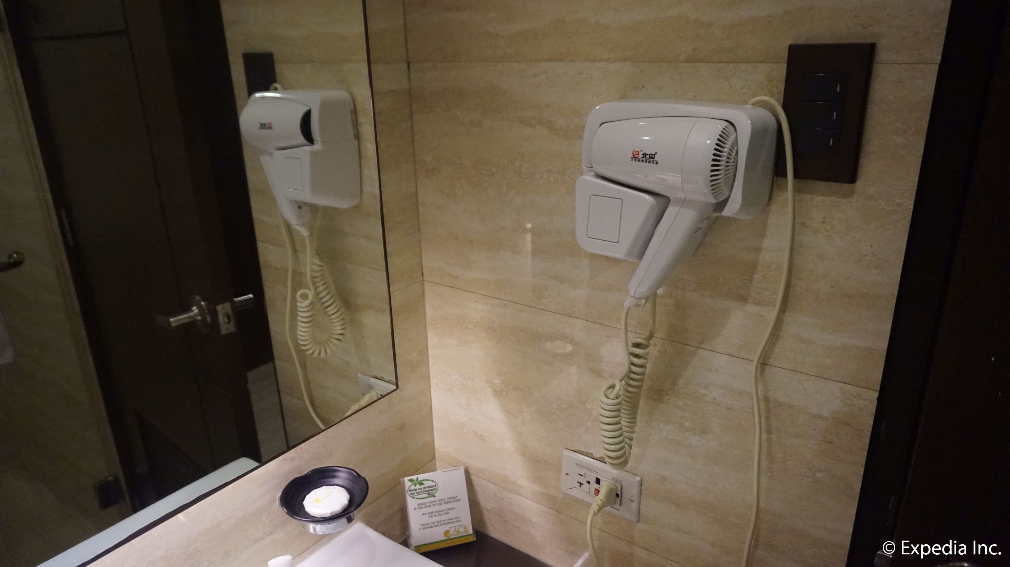 A bathroom with a hairdryer mounted on the wall, a mirror, and a sink with a soap dispenser.