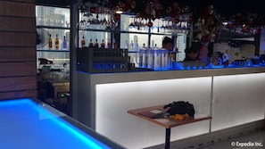 A bar area with shelves of bottles and glasses, a counter with a laptop, and a table with a bag and a notebook. - Ace Hotel & Suites (Pasig)