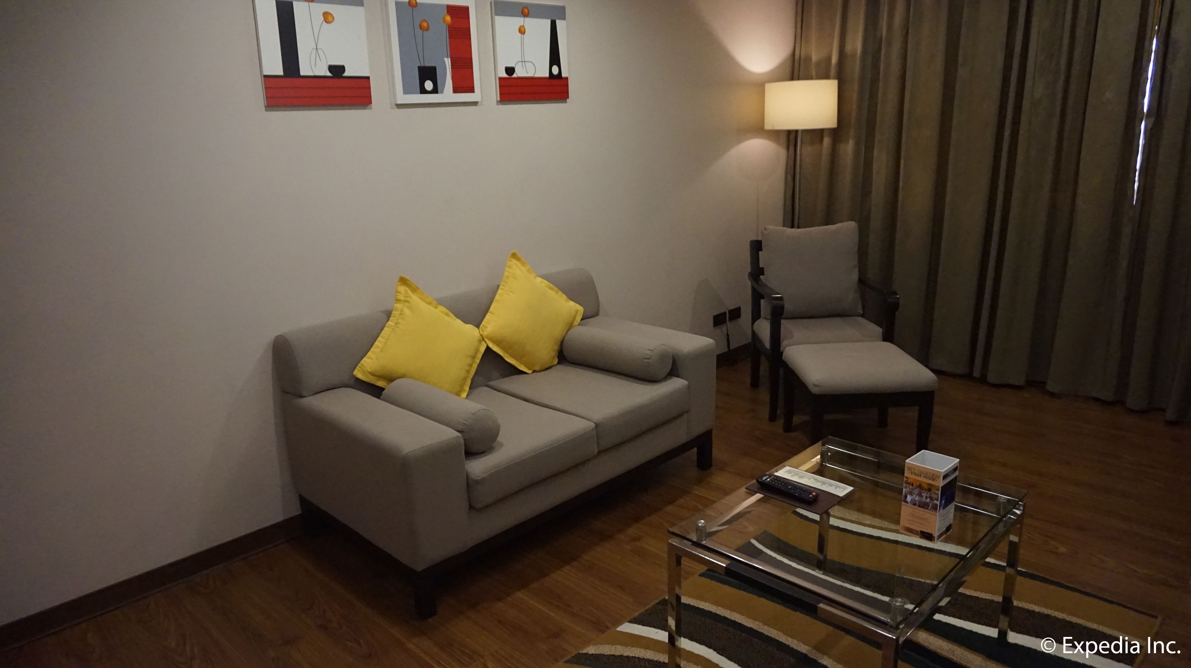 A modern living room with a grey sofa, two yellow cushions, a glass coffee table, a wooden side table, a grey armchair, and a lamp.