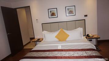 A hotel room with a bed, a bedside table with a phone and a notepad, a door, and two framed pictures on the wall.