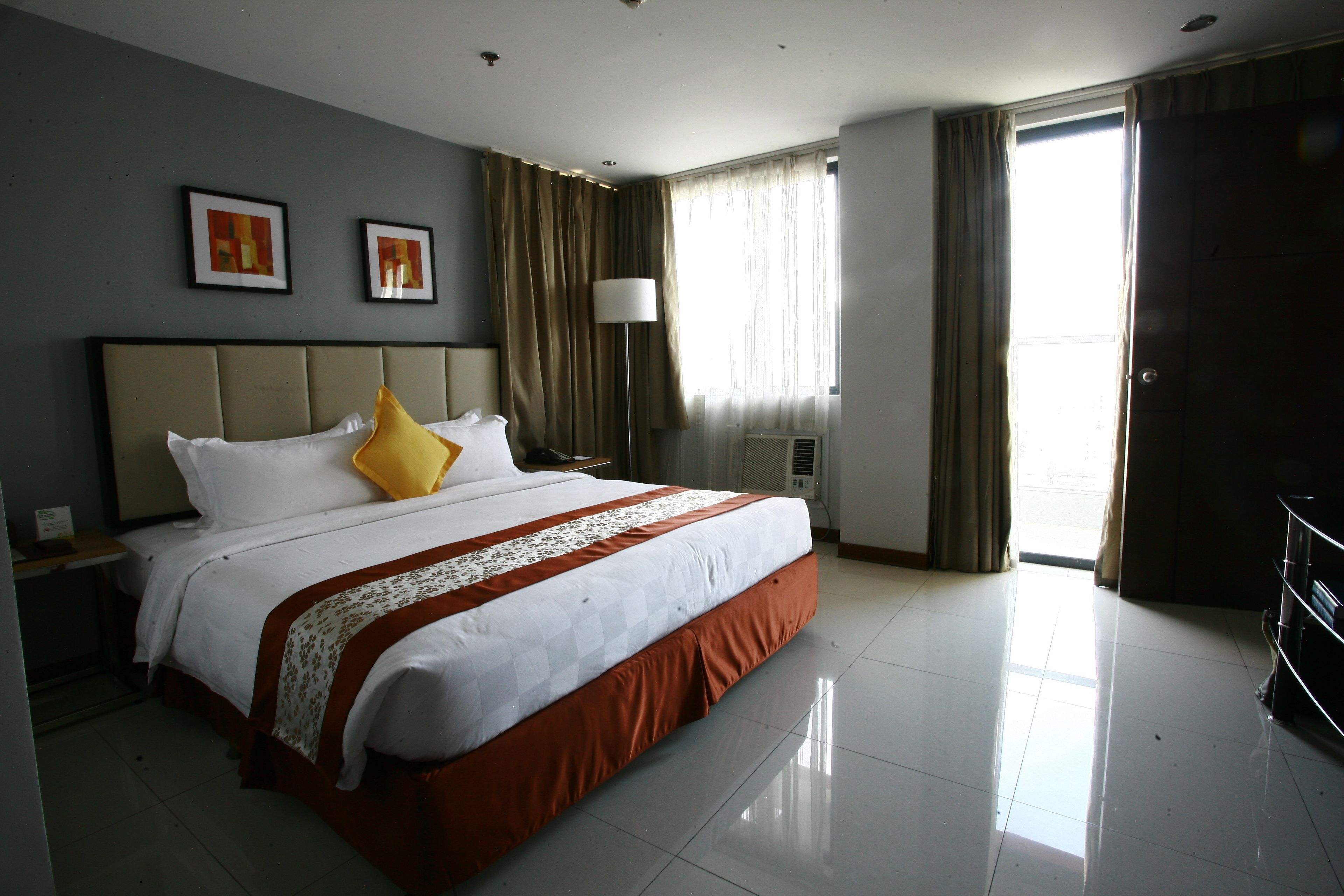 Een hotelkamer met een groot bed, een nachtkastje, een lamp en een raam met gordijnen.